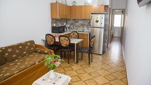 Un espace de vie compact comprenant un canapé, une table à manger, des chaises, un coin cuisine avec un réfrigérateur et un four à micro-ondes, et un sol carrelé.