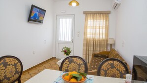 Une chambre d’hôtel compacte comprenant un coin repas, un canapé, une télévision et une fenêtre avec des rideaux.