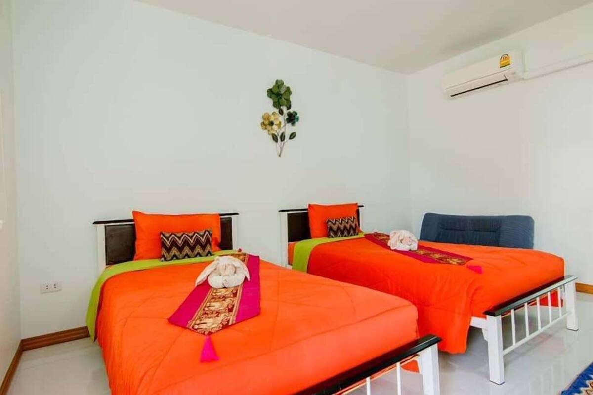 Una habitación con dos camas, cada una con ropa de cama naranja y almohadas decorativas. Hay un aire acondicionado de pared y una pequeña decoración en la pared sobre las camas.