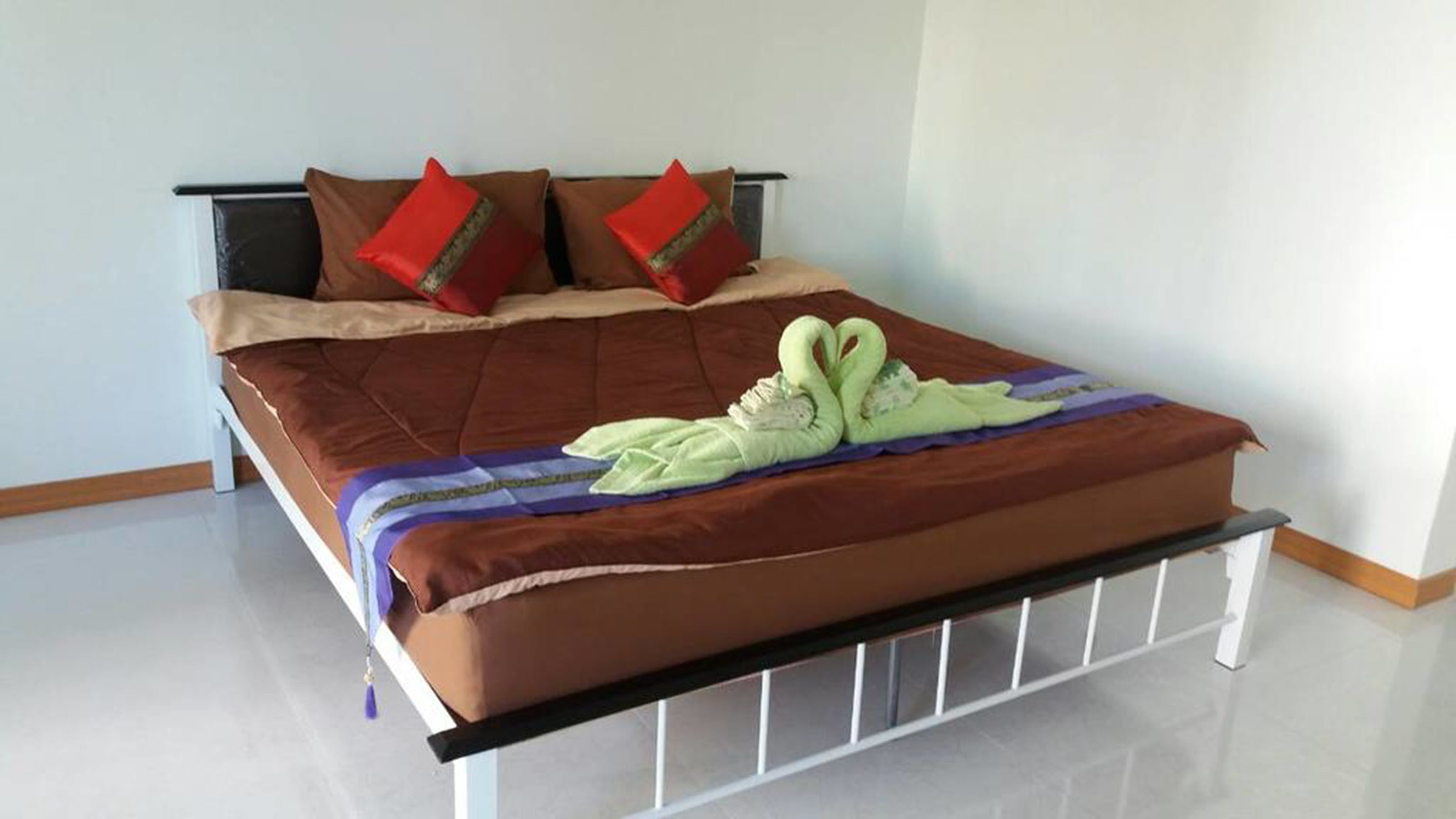 A bed with a brown mattress, two red pillows, and a green towel shaped like swans.