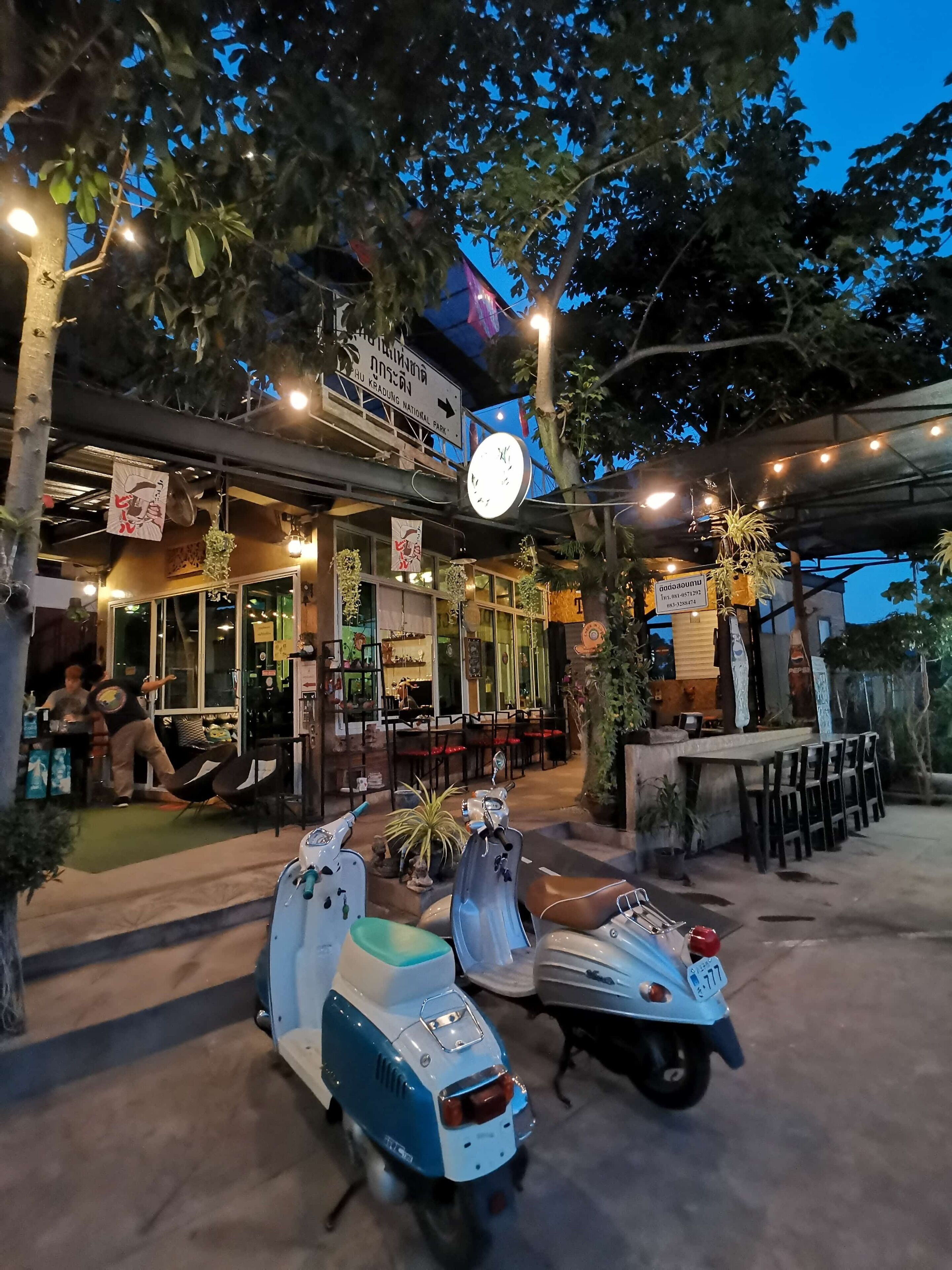 Un restaurante con terraza, un reloj y plantas en macetas.
