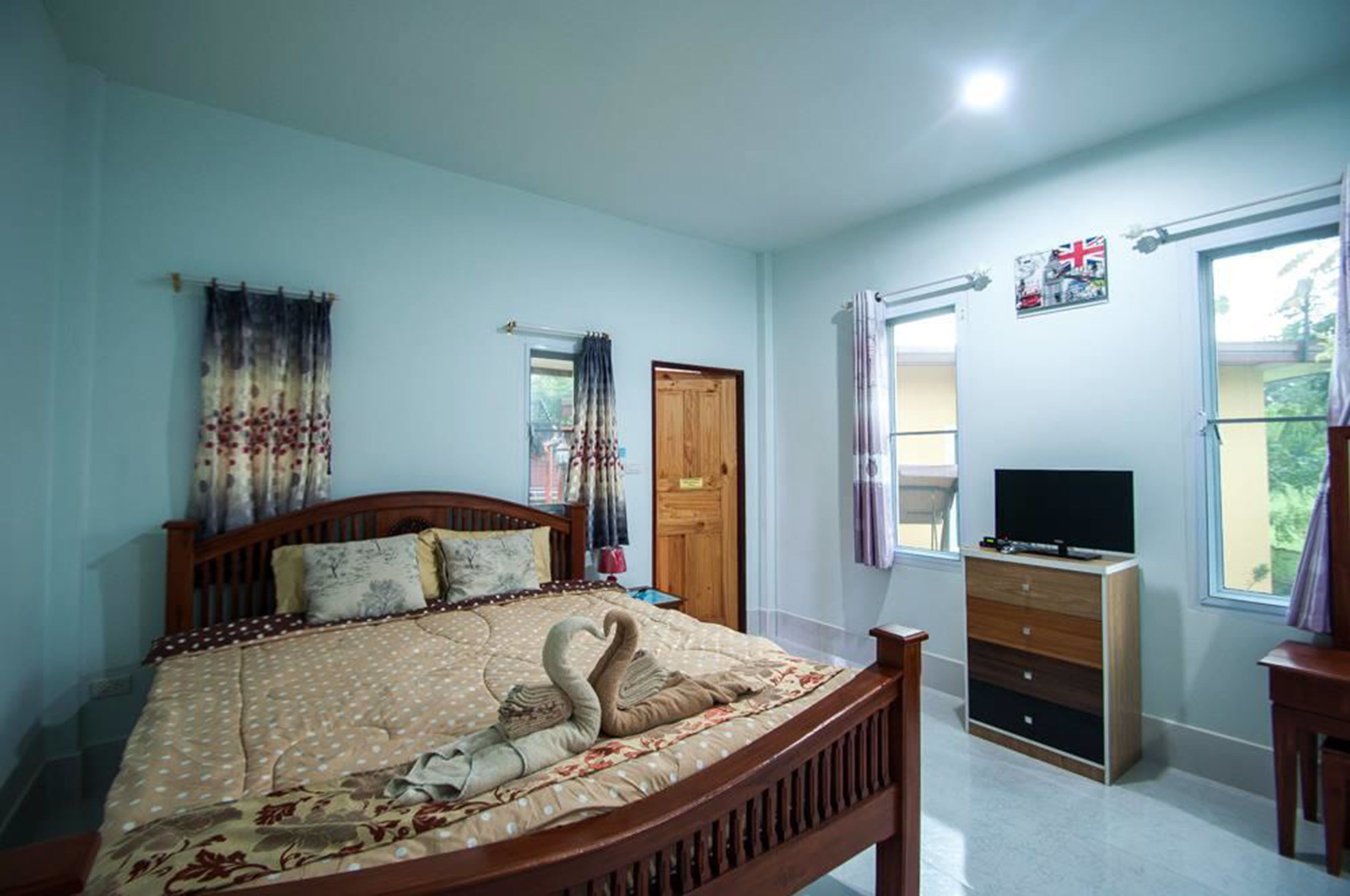 Un dormitorio con una cama de madera, un televisor sobre un mueble de madera y una ventana con cortinas.