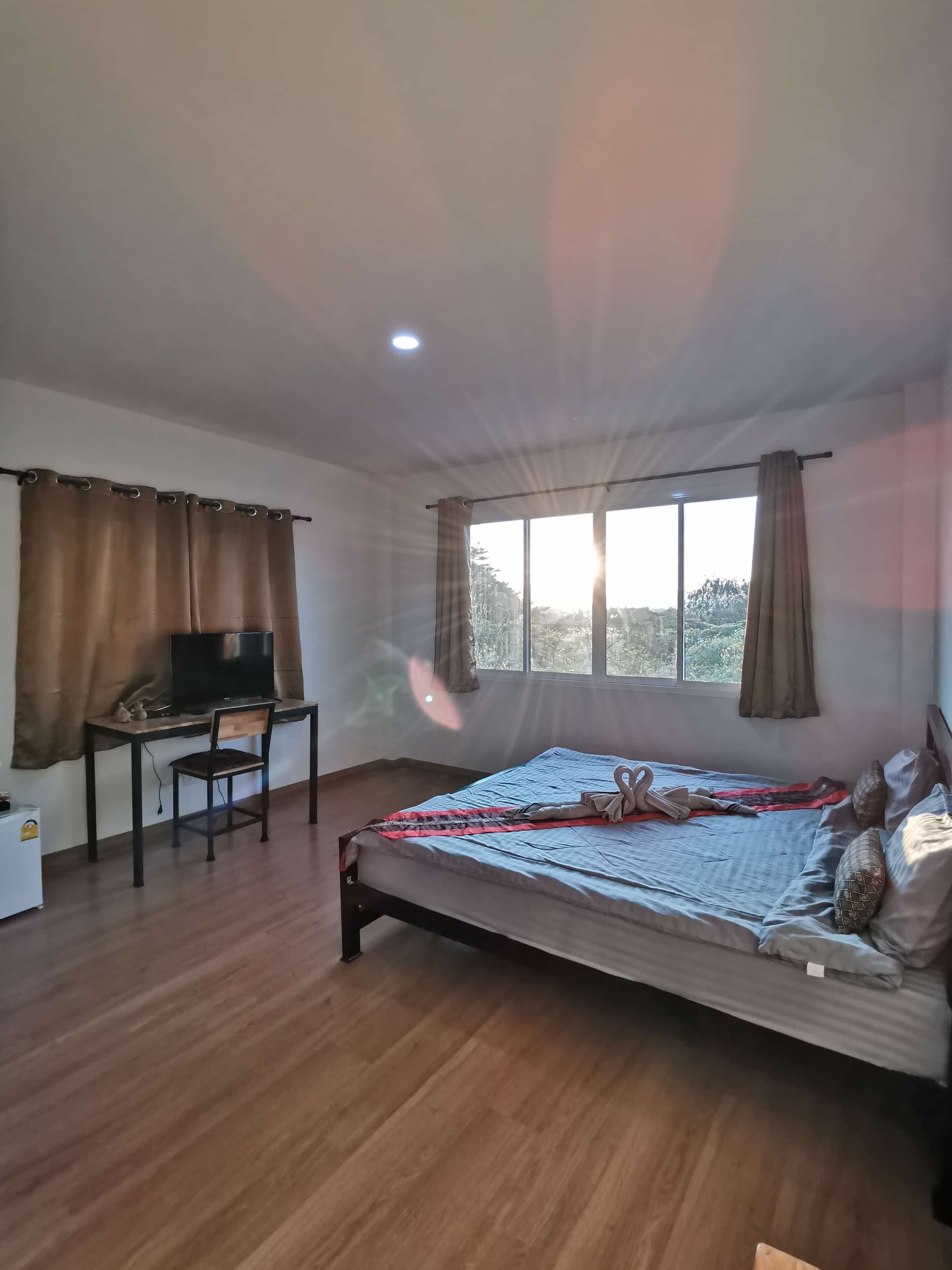 Une chambre à coucher avec un lit, un bureau et une chaise, une télévision et une fenêtre avec des rideaux.