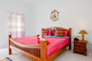 A wooden bed with a red and blue bedspread, a wooden nightstand with a lamp, and a wall decoration of butterflies.