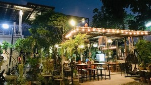 An outdoor seating area with tables and chairs, surrounded by potted plants and a canopy with string lights. - Panida Goodwill (Nong Hin)