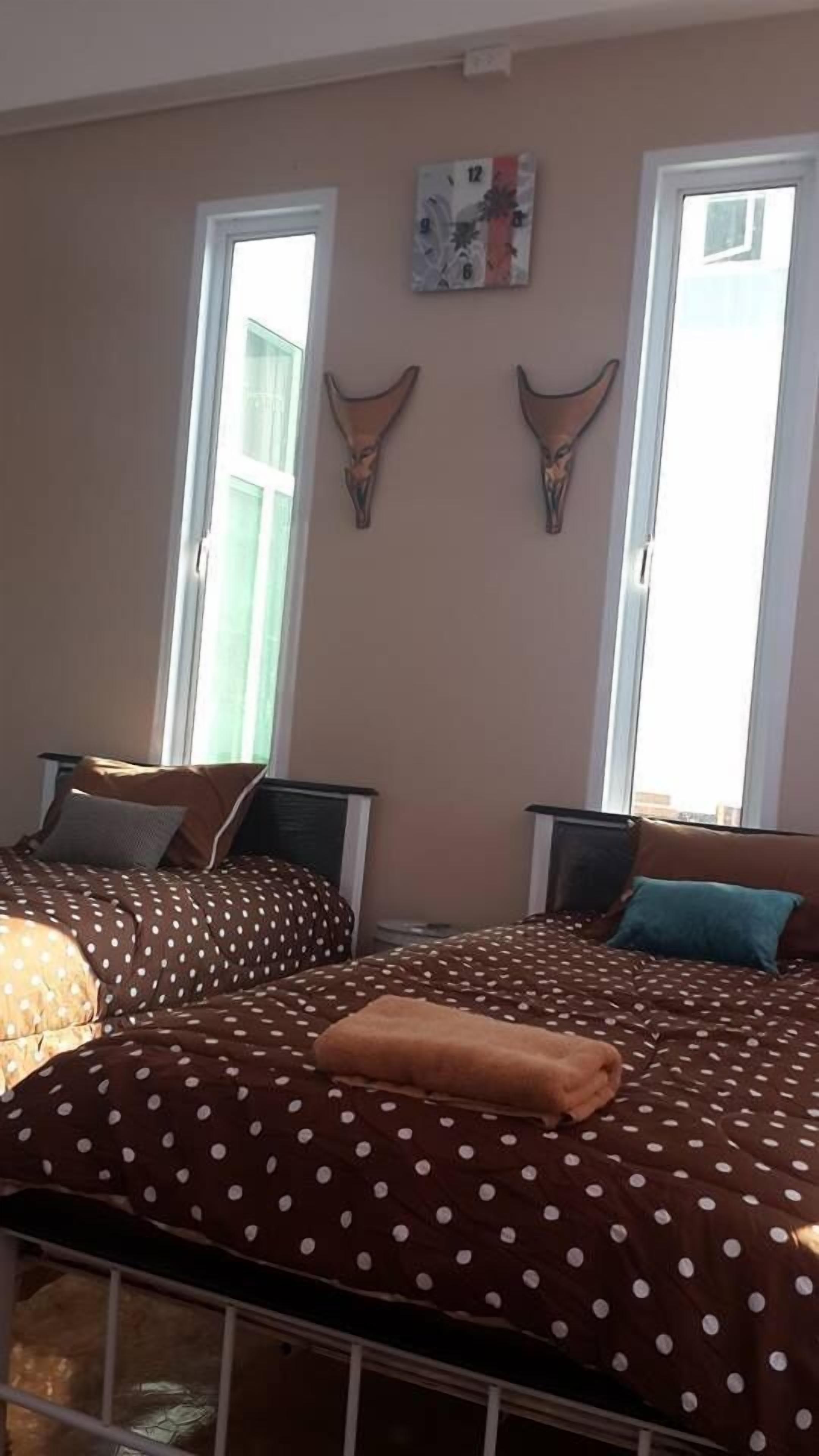 Un dormitorio con dos camas, cada una con una colcha de lunares marrones y almohadas a juego. Se observan dos cráneos de animales colgados en la pared sobre las camas.