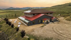 Una casa moderna de dos pisos con techo rojo, rodeada por un camino de grava y un paisaje con césped y colinas al fondo.