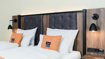 A neatly made bed with white and orange bedding, a dark headboard, and two wall-mounted reading lamps.