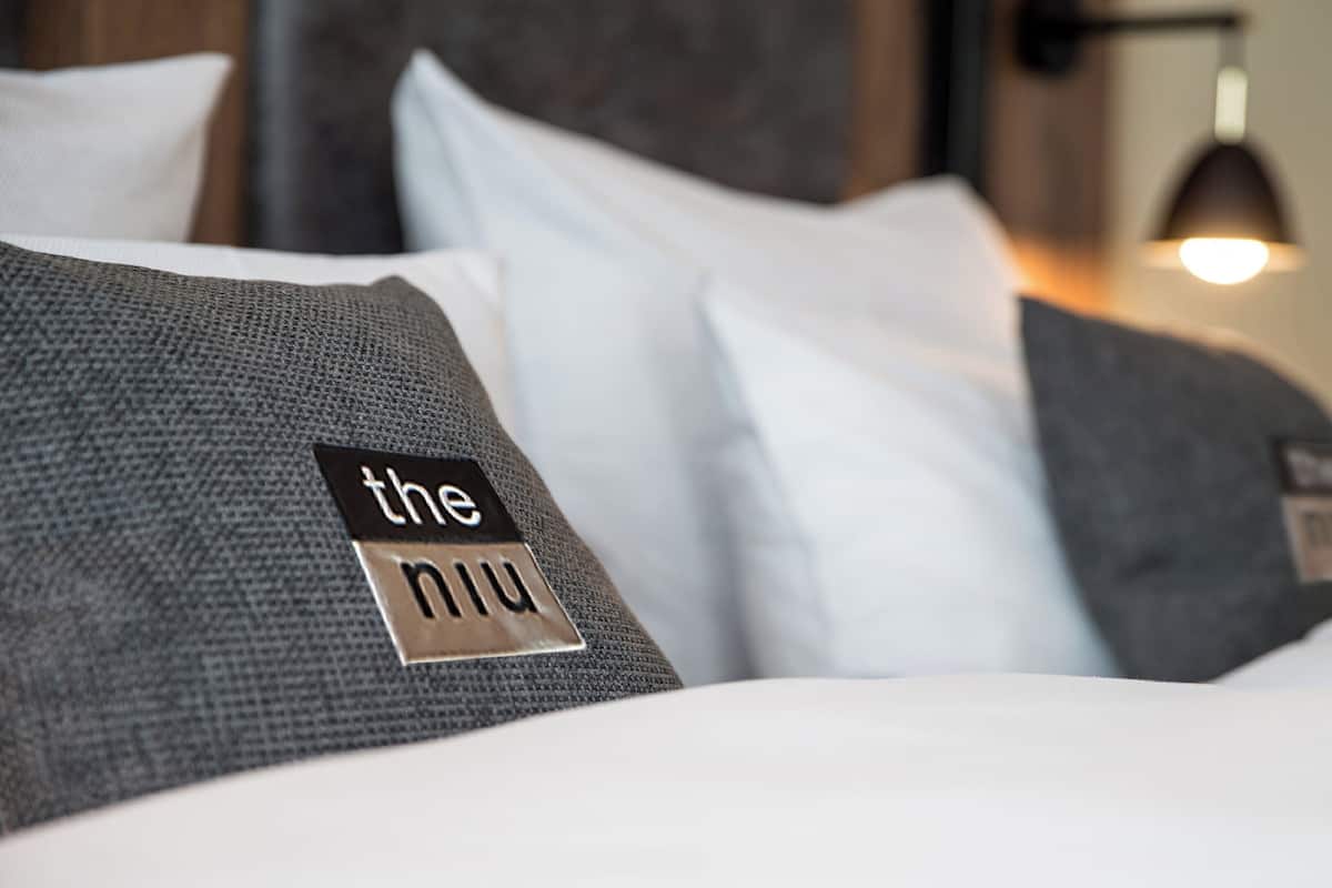 A bed with a gray textured pillow and a white pillow. There is a label on the pillow with the text "the niu".
