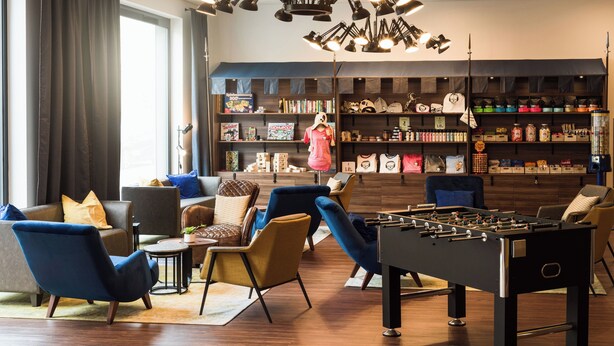 Un salon moderne avec un baby-foot, des sièges confortables, une bibliothèque et une grande fenêtre avec des rideaux.