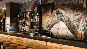 Un espace bar avec des tabourets en bois, un comptoir avec un ordinateur portable et des étagères remplies de bouteilles et de verres.