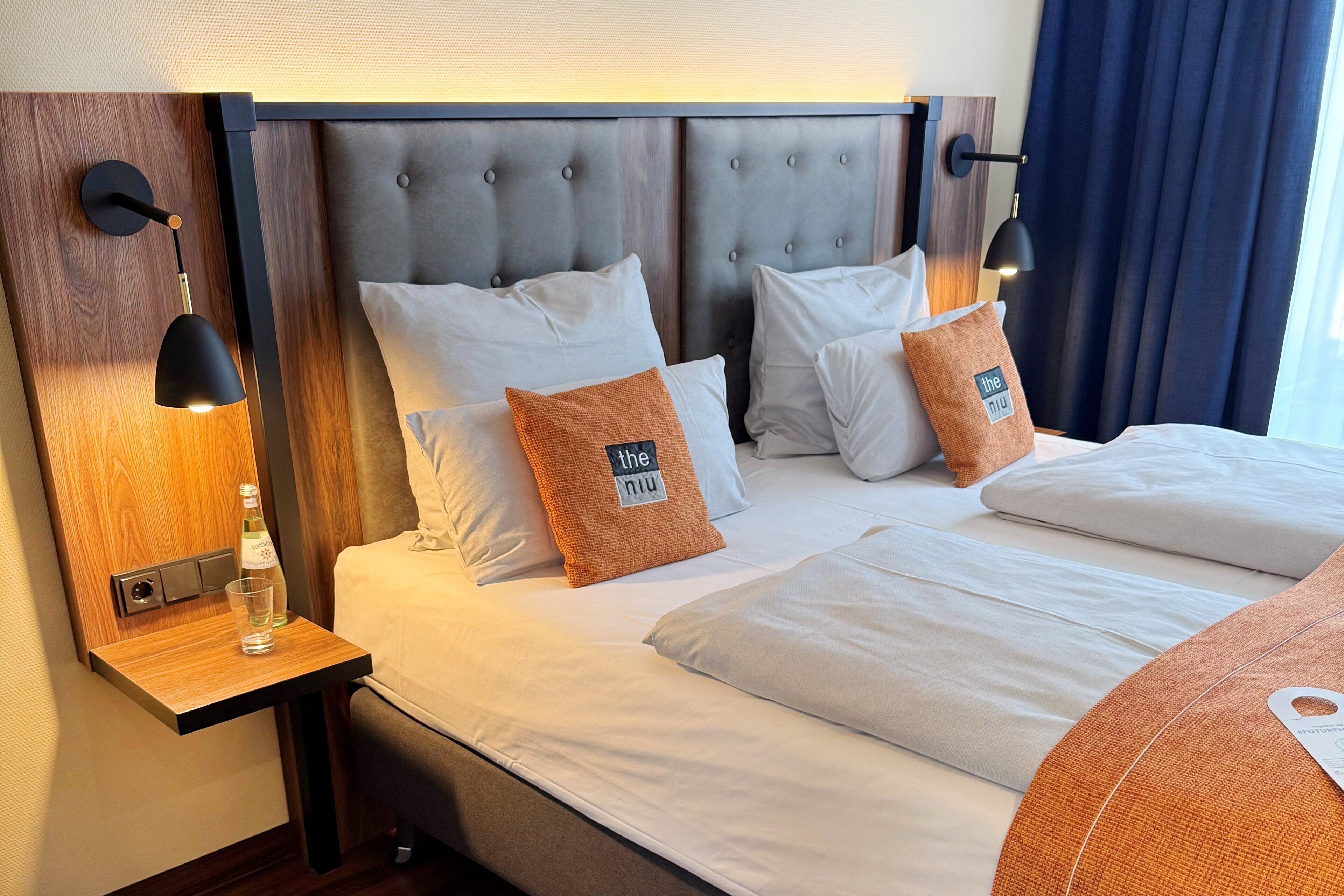 A hotel room with a tufted headboard, white bedding, and two wall-mounted lamps.