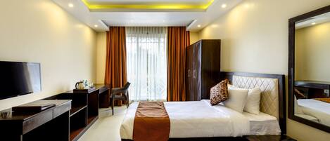 A hotel room with two beds, a desk, a TV, a mirror, and a window with curtains.