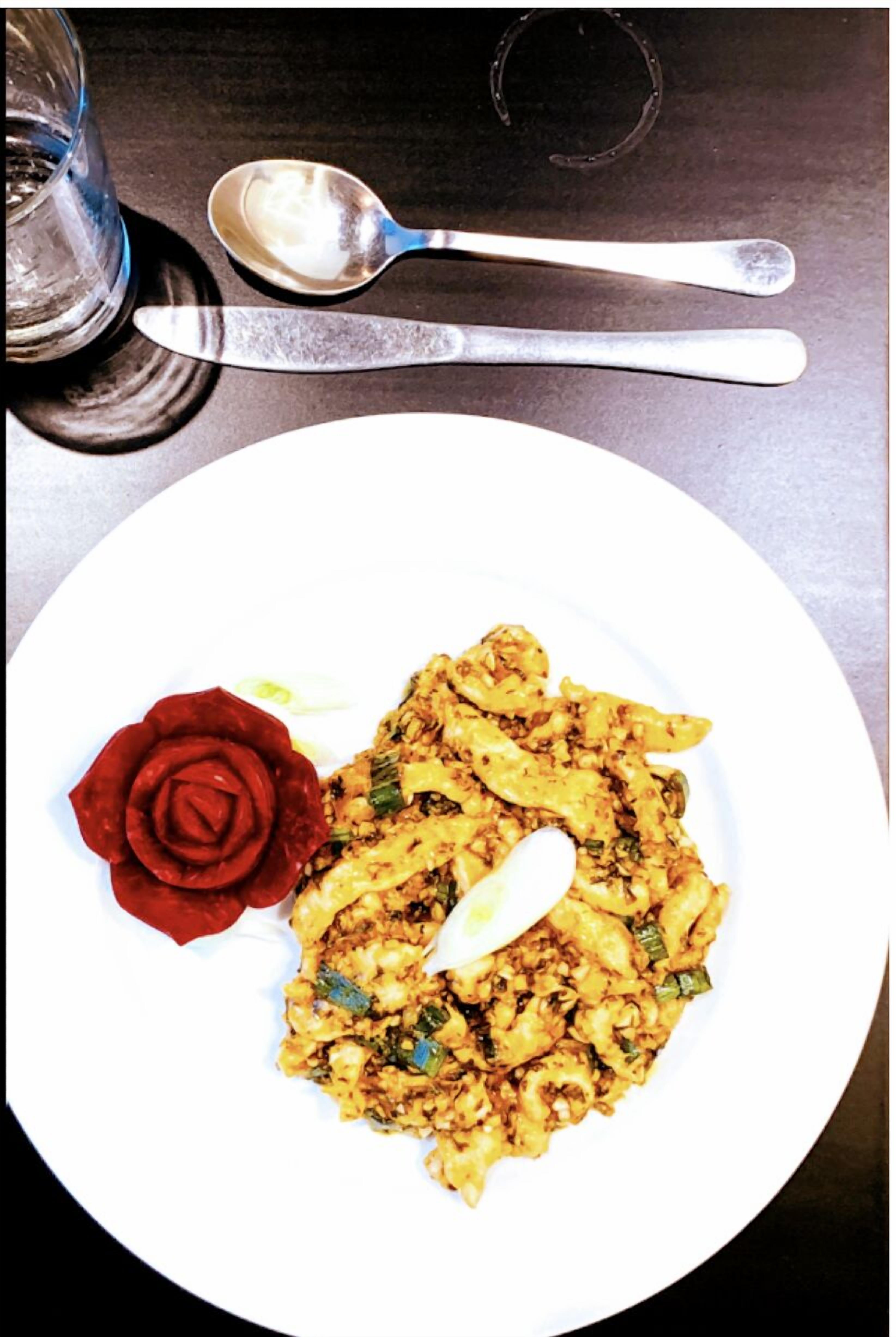 Une assiette de nourriture décorée d’une rose, accompagnée d’une cuillère.