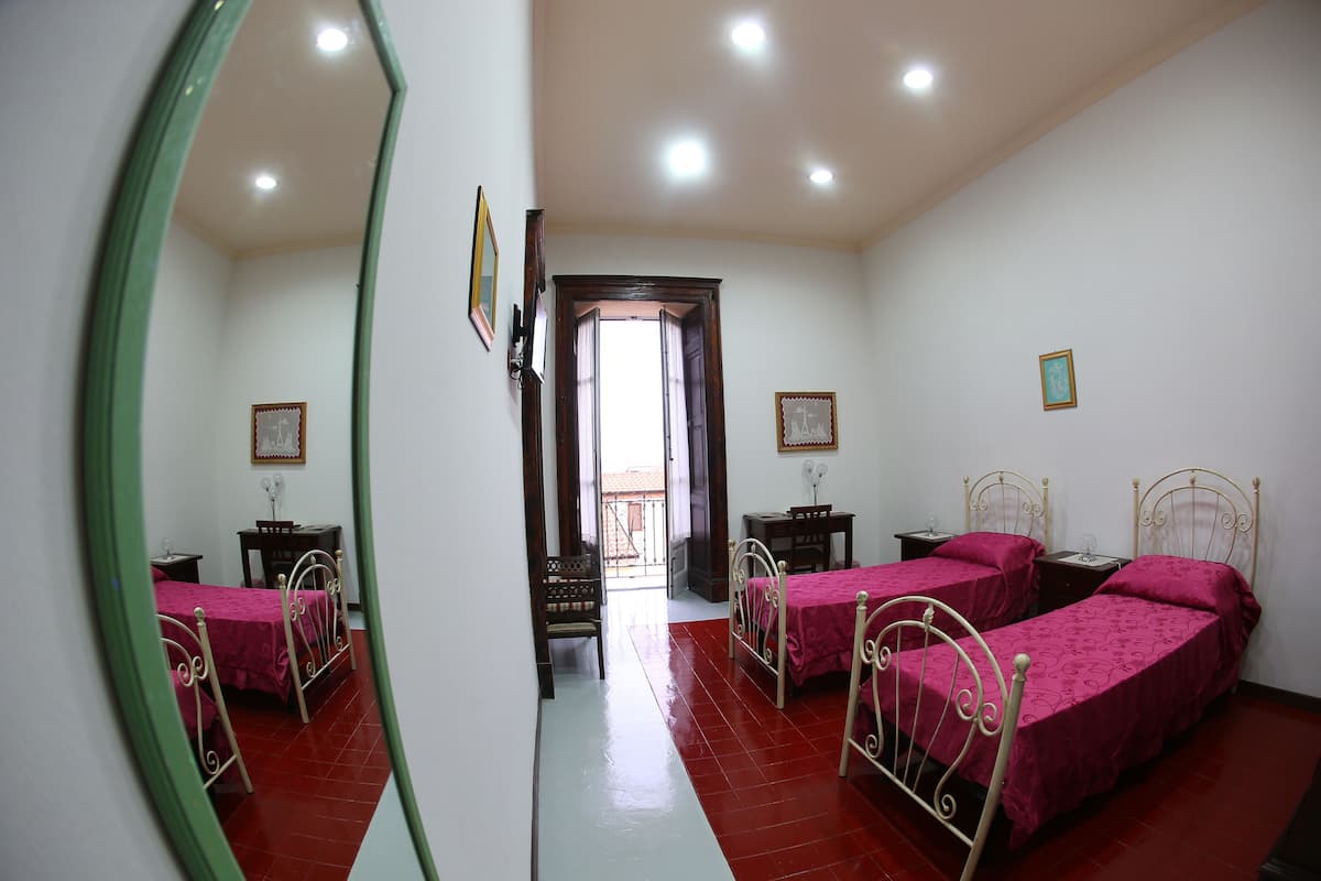 A bedroom with two beds, a mirror, and a door leading to a balcony.