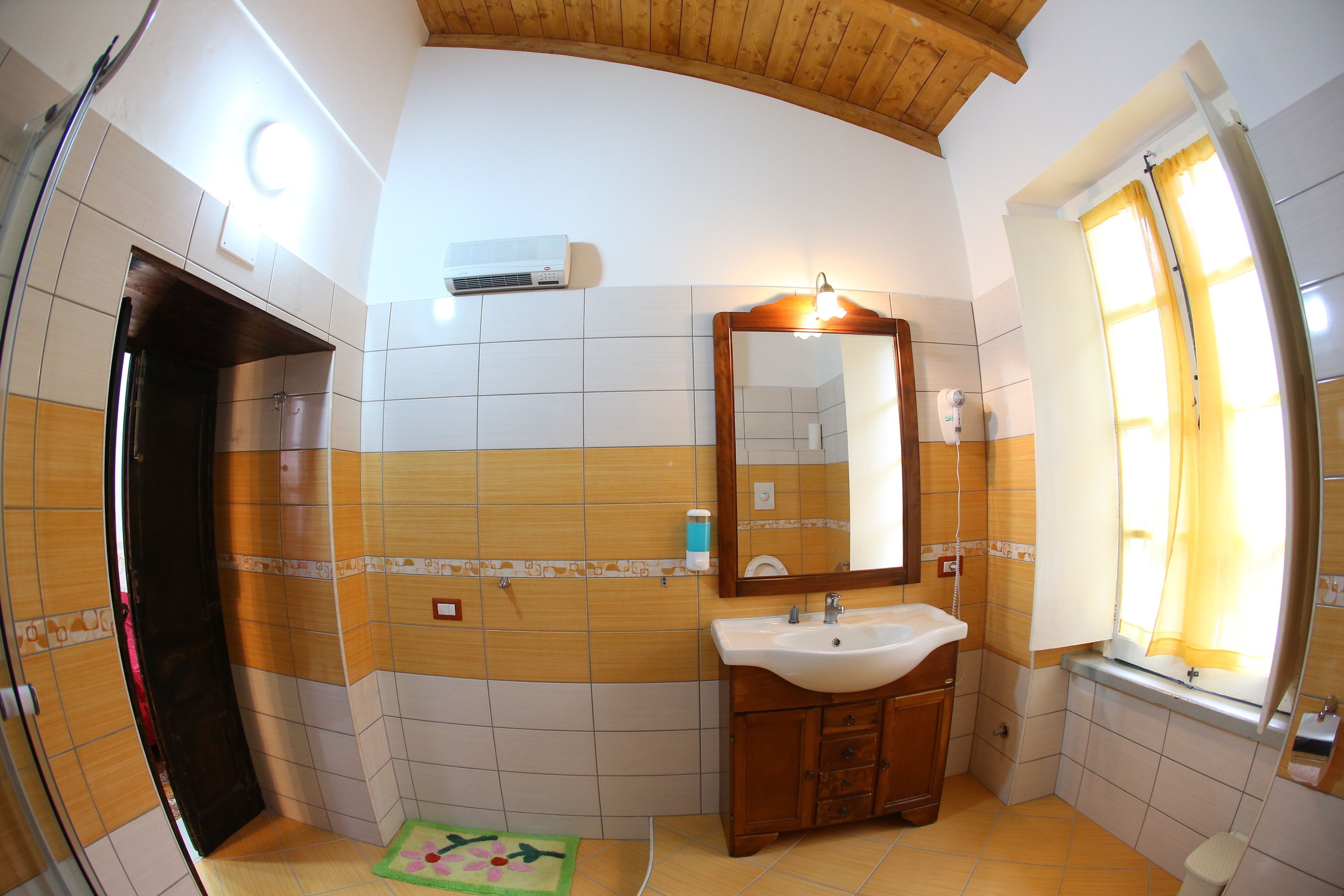 Un baño con techo de madera, un lavamanos, un espejo y una ventana con cortinas.