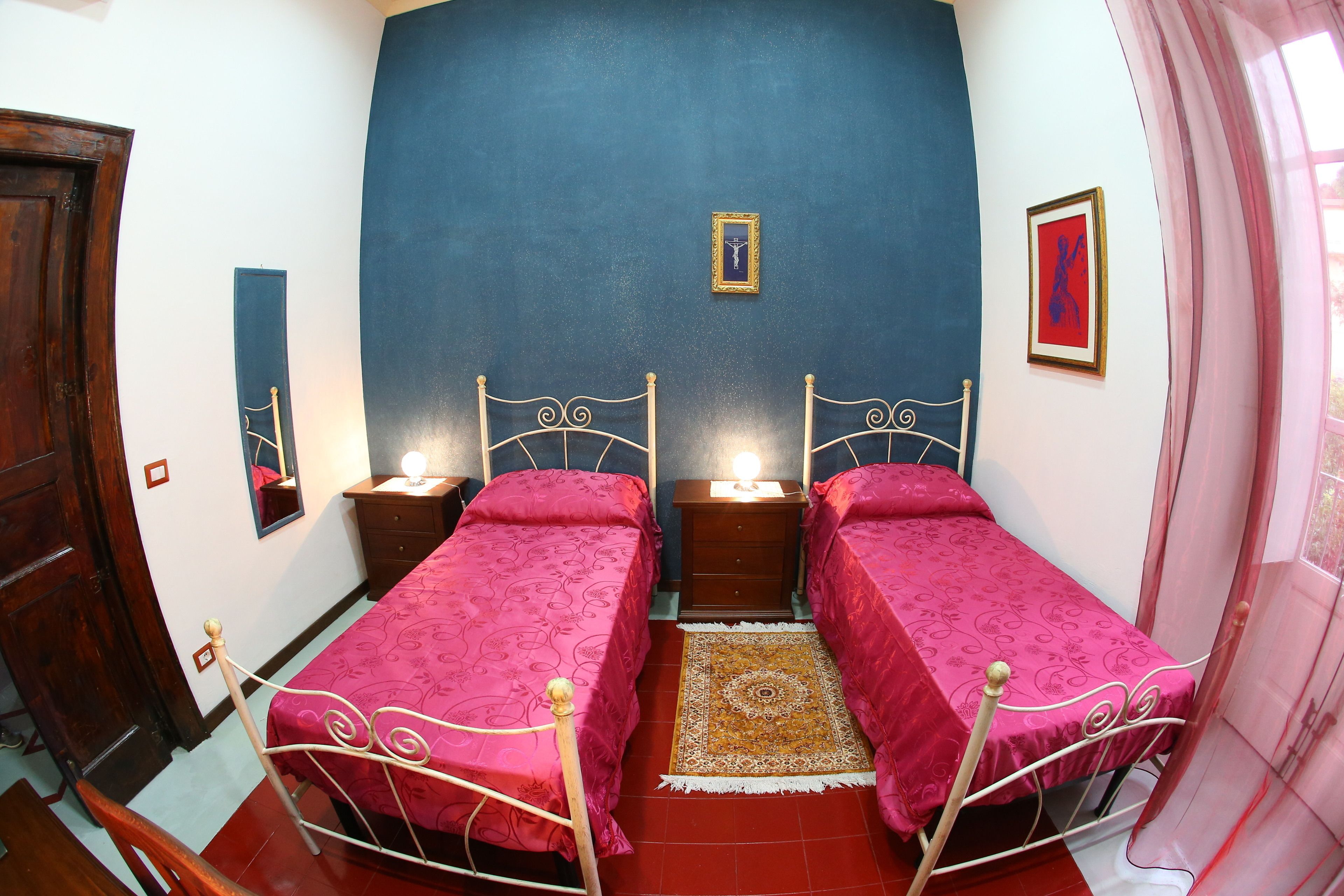 A bedroom with two beds, a nightstand, a mirror, and a window with curtains.