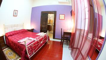 Une chambre avec une couvre-lit rouge, une tête de lit en bois, un petit bureau avec une chaise et une fenêtre avec un rideau rouge.