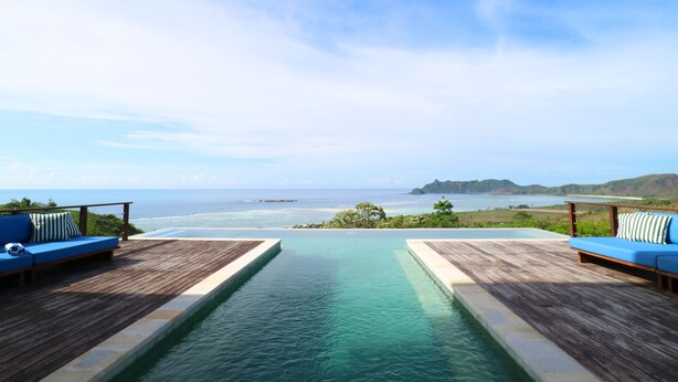 A pool with wooden deck seating and a view of the ocean.