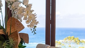 A dining table set with white chairs, a vase of white orchids, and a view of the ocean.