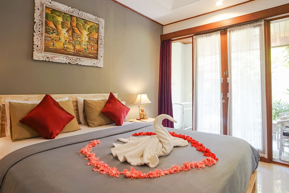 A hotel room with a bed, a painting on the wall, and a balcony with curtains.
