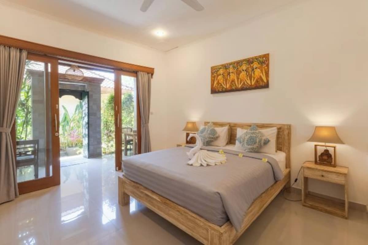 A bedroom with a bed, two bedside lamps, a painting, and a view through a glass door.