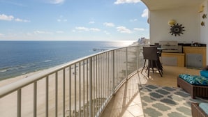 A balcony with a view of the sea, a dining area with a table and chairs, and a kitchen area with a countertop and cabinets. - Turquoise Place 1206D by Liquid Life (Orange Beach)