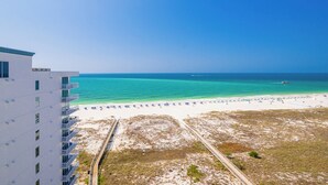 A beach view with a white building, a sandy beach, and a clear blue sky.