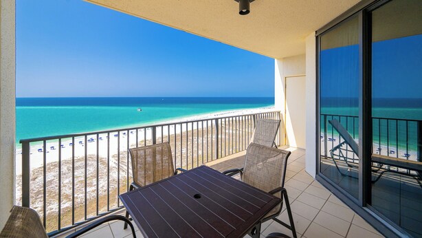A balcony with a view of the beach and ocean, a table, and two chairs.