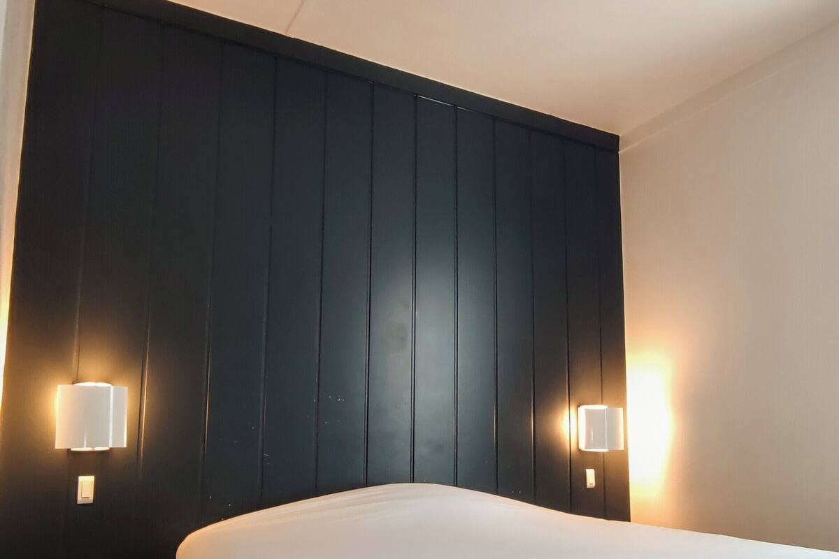A hotel room with a large bed, dark wood headboard, and two wall-mounted lamps.