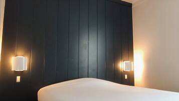 Habitació d'hotel amb un llit gran, un panell de capçal de fusta fosca i dues làmpades penjades a la paret.