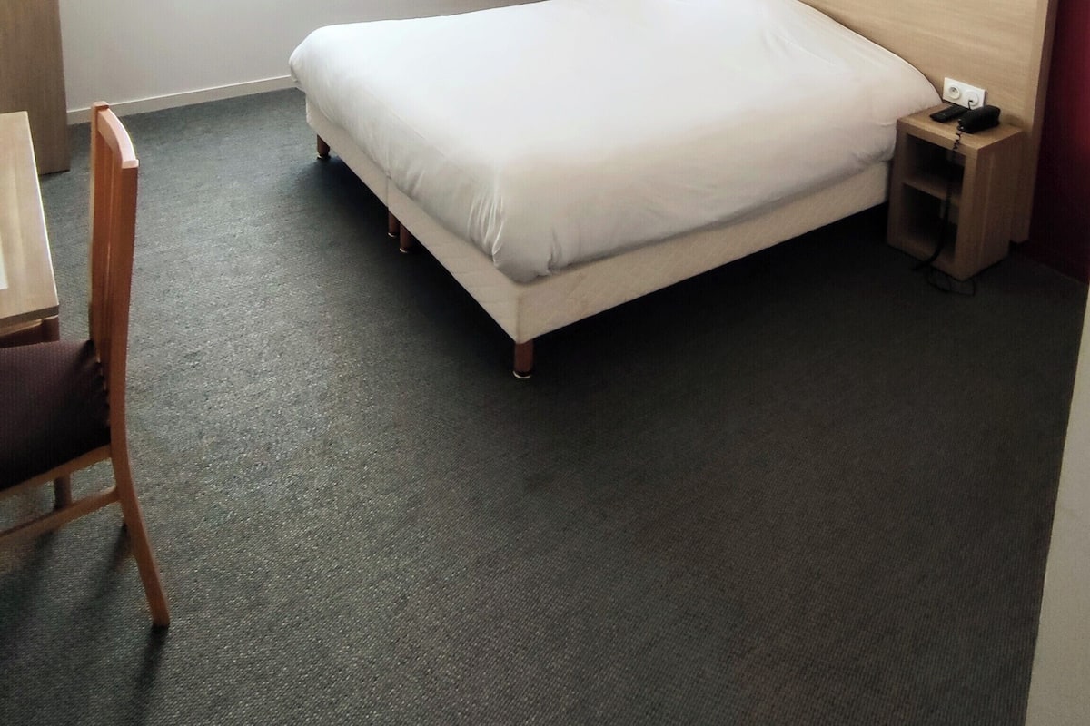 A hotel room with a bed, a desk, a chair, and a nightstand.