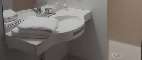 Un baño moderno con un lavabo blanco, espejo y perchero. Hay dos secamanos y un cubo de basura.