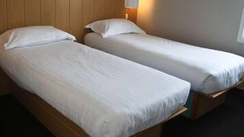 Dos camas individuales con cabeceros de madera y ropa de cama blanca en una habitación con pared de madera y una lámpara de pared.