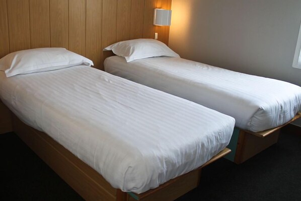 Two single beds with wooden headboards and white bedding in a room with a wooden wall and a wall-mounted light. - Fasthotel Laval (Laval)