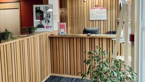 Un área de recepción con un panel de pared de madera, un mostrador de recepción, una computadora y un cartel publicitario de un hotel.