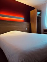 Una habitación de hotel con una cama grande, un cabecero de madera y un armario empotrado.