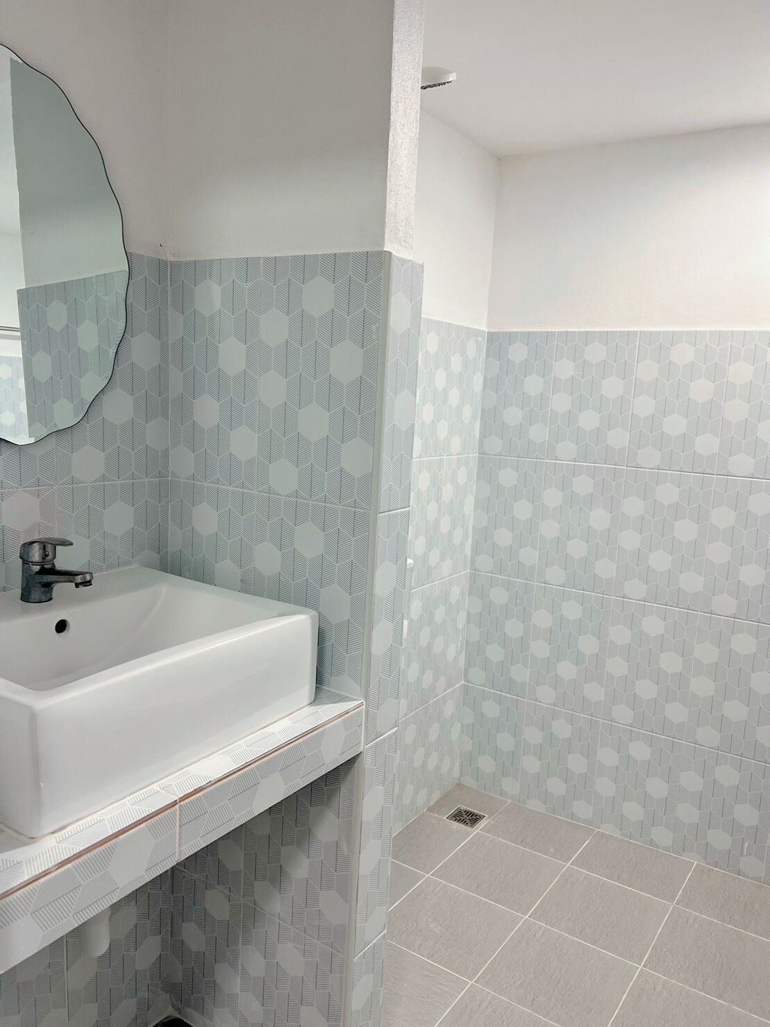 A bathroom with a white sink, a mirror, and patterned hexagonal tiles on the walls and floor.