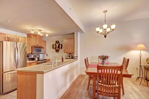 Una cocina moderna con armarios de madera, electrodomésticos de acero inoxidable, una isla central y un comedor con sillas y mesa de madera.