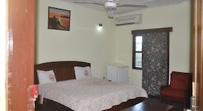 A bedroom with a bed, a chair, a desk, a ceiling fan, an air conditioner, a window with curtains, and a painting on the wall. - Hotel President (Accra)