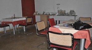 A dining area with tables and chairs, a small table with a checkered tablecloth, and a wall with a red panel. - Hotel President (Accra)