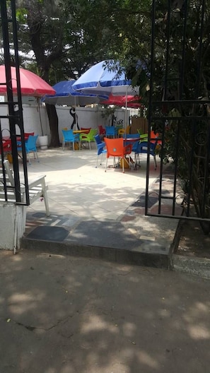 An outdoor seating area with colorful chairs and umbrellas, surrounded by trees and a metal fence. - Hotel President (Accra)