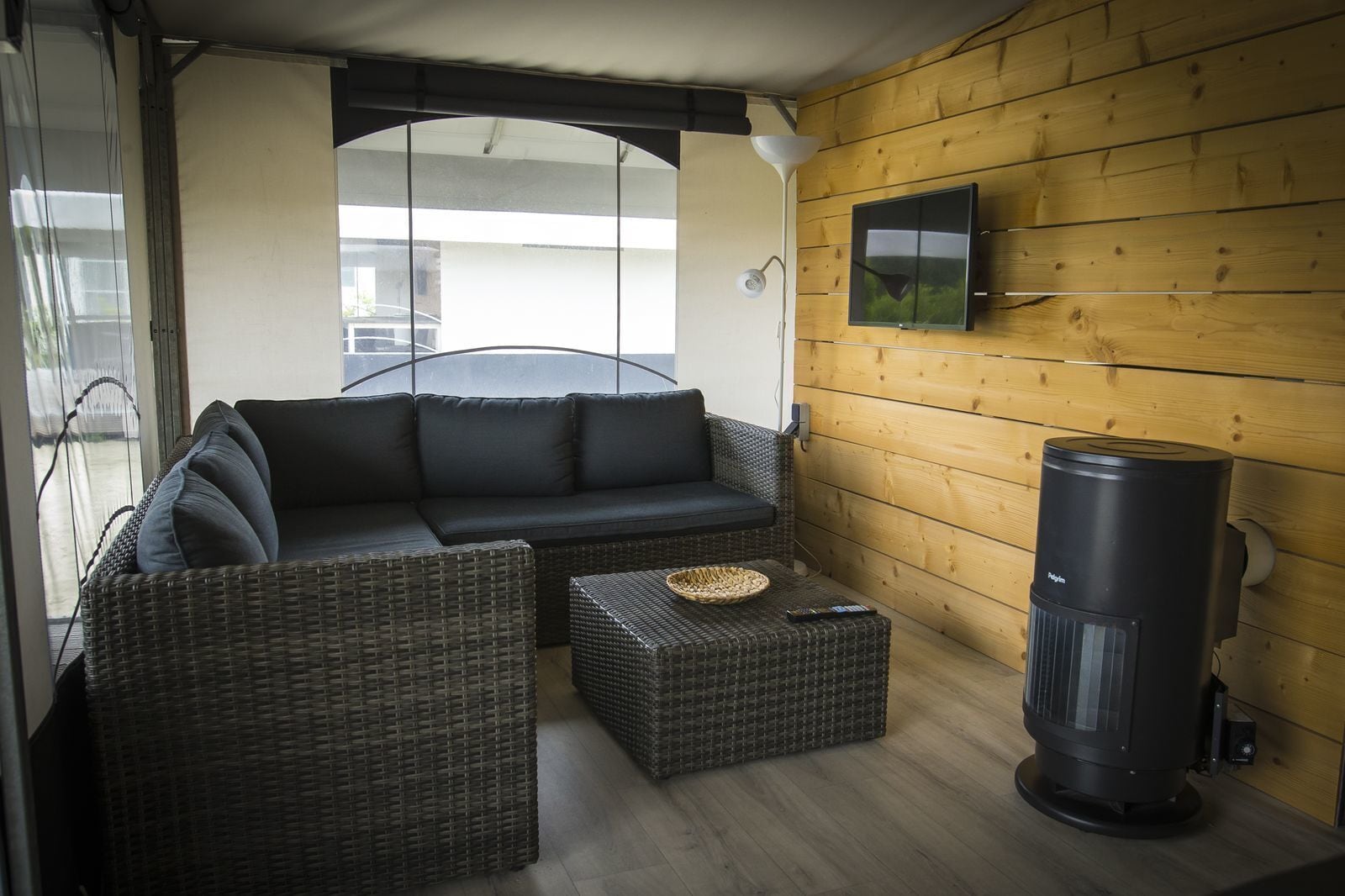 A cozy room with a dark-colored sofa, wicker furniture, a flat-screen TV, and a wood-burning stove.