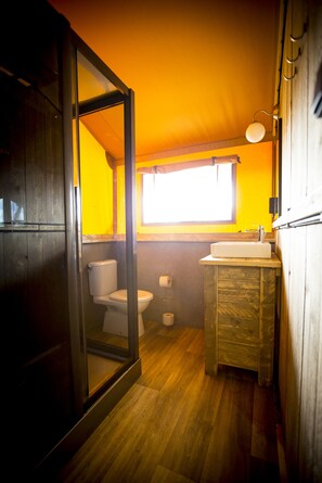 A compact bathroom with a wooden floor, a white toilet, a sink, and a window providing natural light.