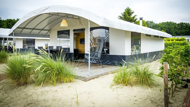 Una casa moderna frente a la playa con un porche cubierto, mobiliario exterior y un entorno de arena.