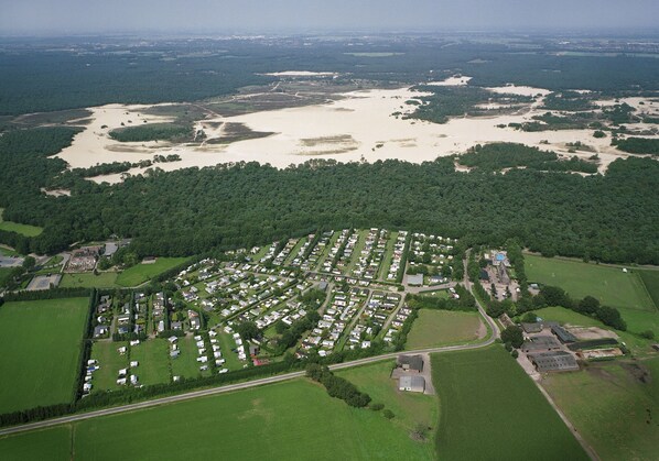 An aerial view of a campground with RVs and tents, surrounded by green fields and a large water body.