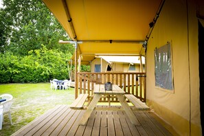 A wooden deck with a picnic table and chairs, a covered area with a railing, and a view of a lush green garden.