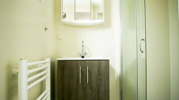 A bathroom with a white radiator, a wooden cabinet, a glass shower enclosure, and a mirror above the sink.