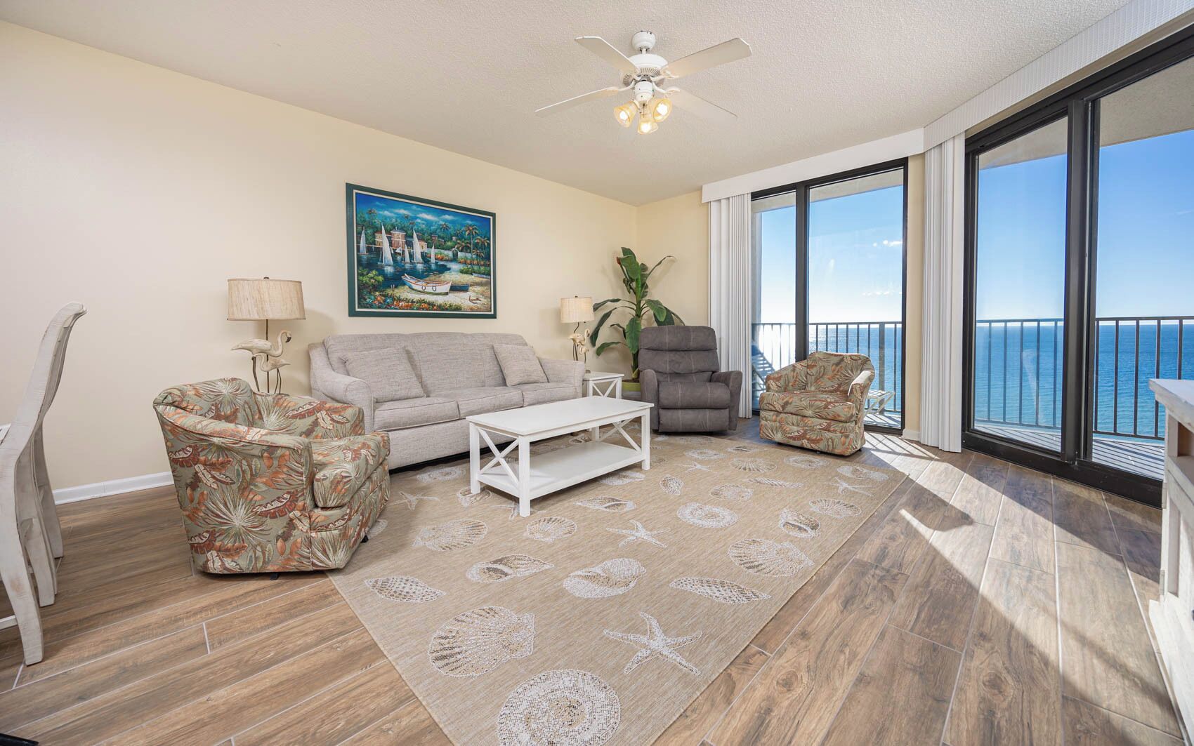 A living room with a sofa, armchairs, a coffee table, and a large window with a view of the ocean.