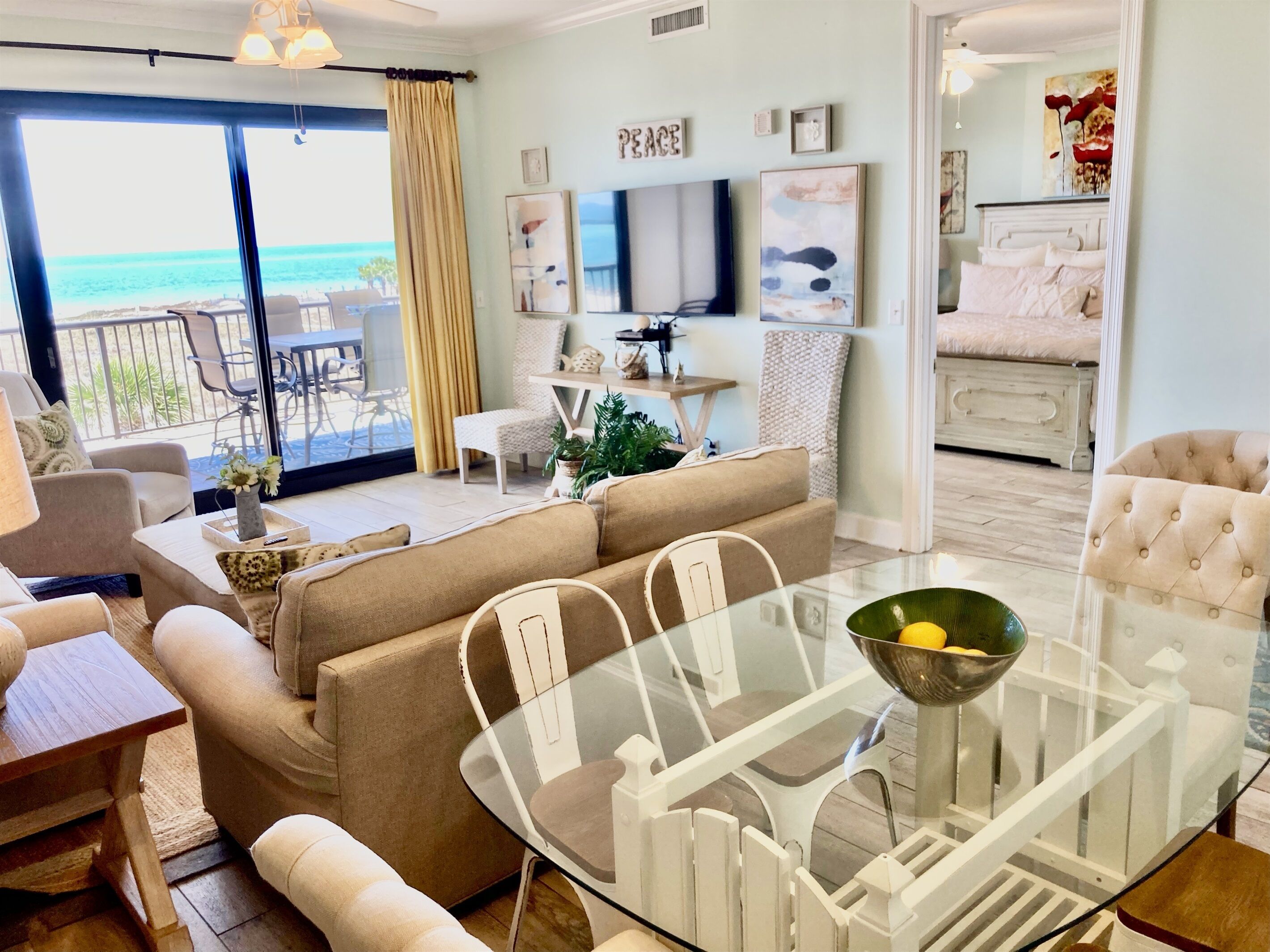 A modern living room with a glass dining table, beige sofas, and a view of the ocean.